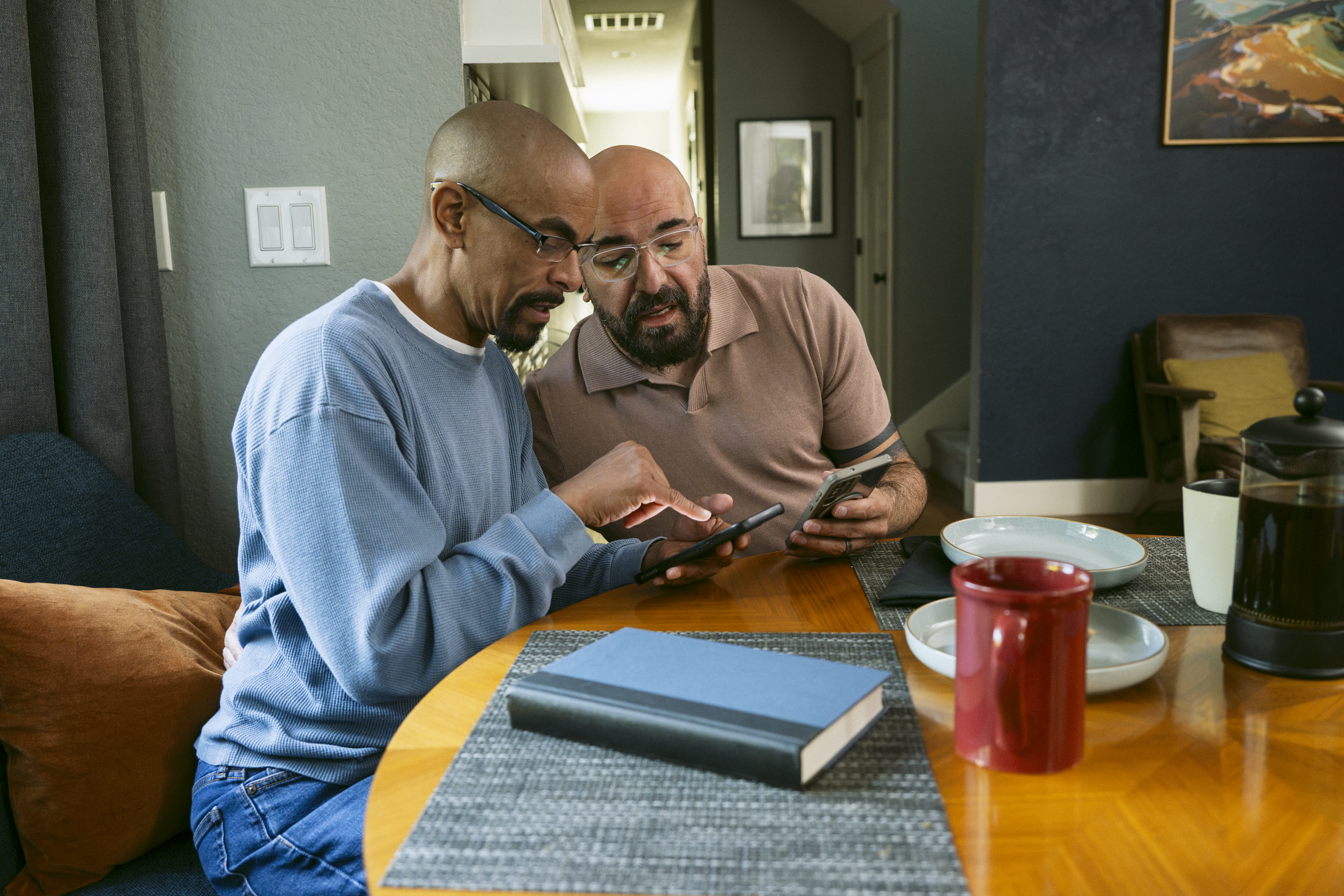 Dos hombres mirando sus teléfonos mientras están sentados a la mesa del comedor.